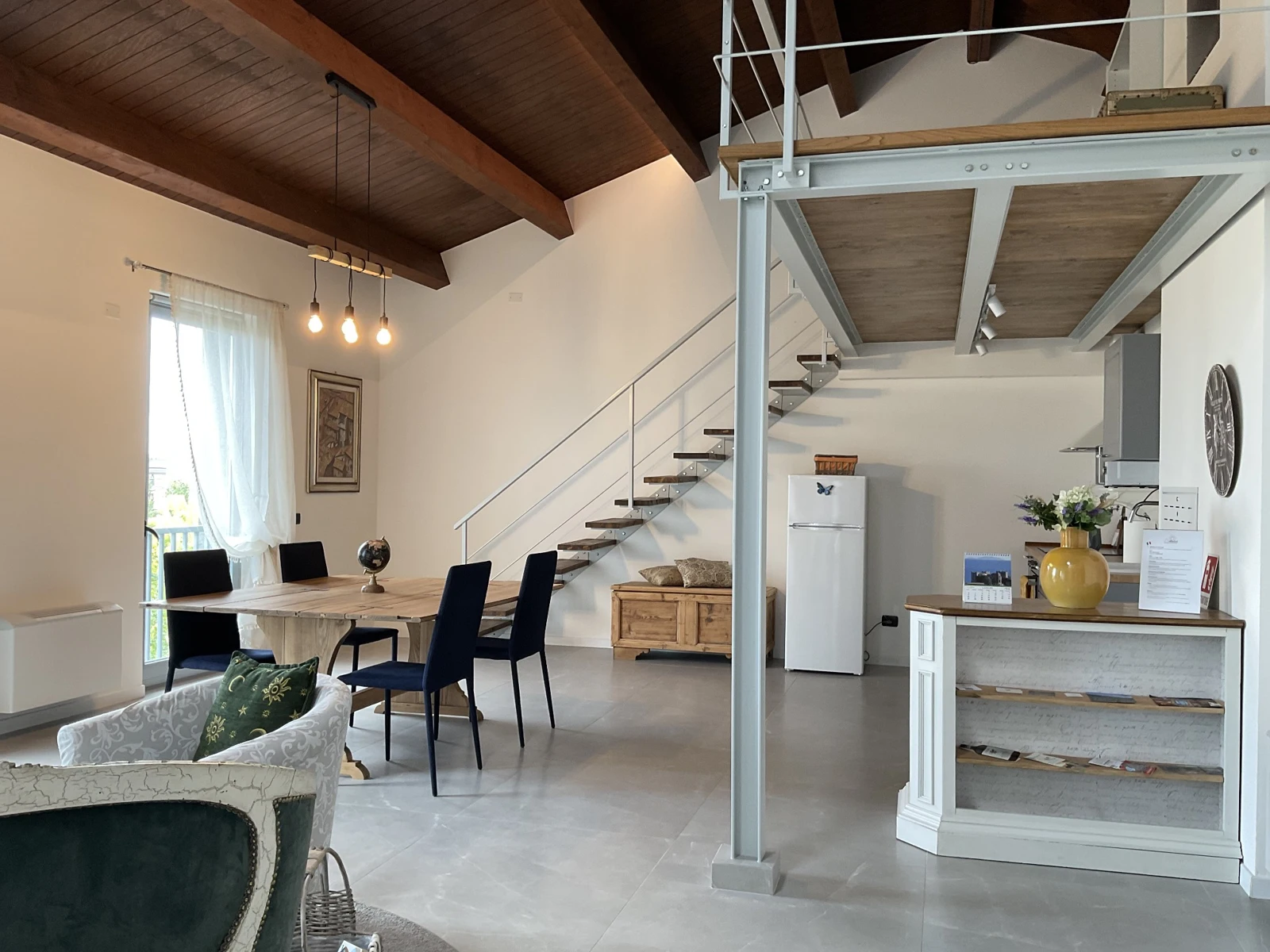 Vista d’insieme dello spazio giorno condiviso, con tavolo, cucina e scala